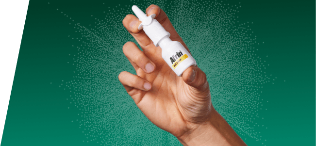 hand holding Afrin nasal spray bottle on green background